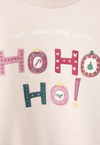 Maglione rosa chiaro con lettere ricamate colorate "HO HO HO!" e palline decorative, inclusi bastoncini di zucchero e motivi di agrifoglio.