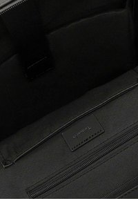 Intérieur d'un sac en tissu noir avec une poche zippée, texture lisse, et une petite étiquette de marque cousue sur la doublure.