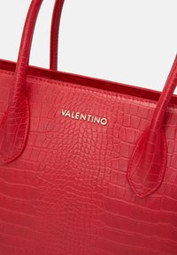 Röd läder tote-väska med krokodilstruktur och guld "Valentino"-logotyp. Har två handtag och en strukturerad design.
