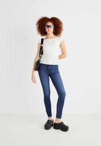 Vit åtsittande topp med korta ärmar, mörkblå skinny jeans och svarta plattformsträskor. Noterbara klara solglasögon och en svart axelväska.