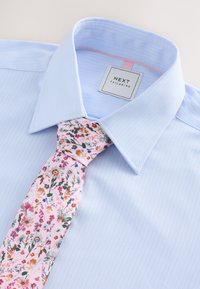 Ljusblå randig skjorta med en rosa blommig slips. Skjortan har en klassisk krage och en etikett märkt "NEXT TAILORING."