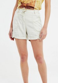 Pantaloni corti beige chiaro con vestibilità rilassata, vita elastica e cordoncino. Presentano tasche laterali e orli ripiegati. Realizzati in tessuto traspirante.