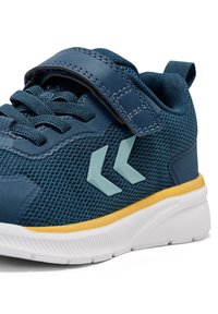 Blå mesh sportssko med velcrolukning, lyseblå accenter, gul mellemsål og hvid gummisål, med en struktureret overside.