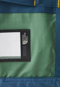 North Face bagasjen i interiøret har et grønt rutemønster i stoffet, et svart merke med hvite logoer, og en blå teksturert fôr.
