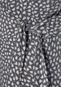 Modrá a bílá vzorovaná látka s jemnou strukturou. Obsahuje detail s uvázaným pasem a nepravidelnými, listovými tvary v opakujícím se vzoru.