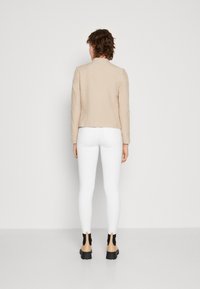Beige cropped blazer made of smooth fabric, paired with white leggings, featuring a tailored fit and subtle shoulder structure.