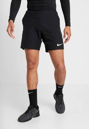 Pantalones cortos deportivos negros de Nike con bolsillos laterales, cinturilla elástica y un logo blanco. Llevados con calcetines deportivos negros y zapatillas.