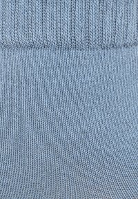 Calzino lavorato a maglia azzurro chiaro con polsino a coste. Il tessuto ha una texture liscia e un motivo di punto uniforme, evidenziando flessibilità e comfort.