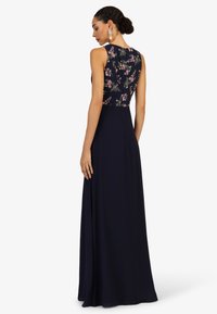 Langes marineblaues Kleid mit einem figurbetonten Oberteil mit floralem Muster und ärmellosem Design, das in einen glatten, ausgestellten Rock übergeht.