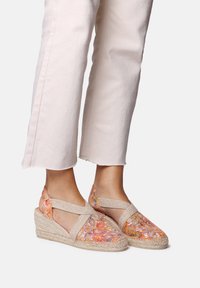 Espadryle na koturnie z materiału w kwiatowy wzór w odcieniach pomarańczowym i pastelowych. Posiadają krzyżujące się paski oraz podeszwę owiniętą jutą.