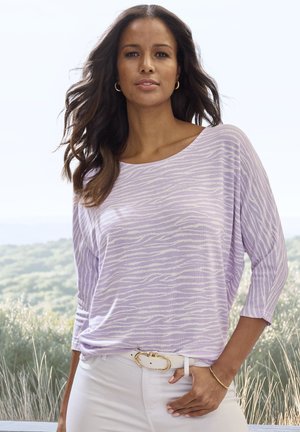 Light purple top with white zebra stripes, relaxed fit, wide boat neckline, 3/4 sleeves, paired with white pants and a gold-accented white belt.