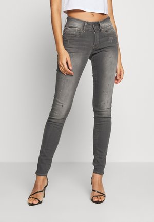 Jeans gris ajustados con ligero desgastado, diseño de cinco bolsillos y una textura suave. Combinados con tacones negros de tiras y una blusa blanca corta.