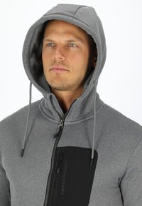 Grijze hooded sweatshirt met een ritssluiting aan de voorkant, zwarte borstzak en trekkoord. Soepele textuur met een casual ontwerp.