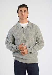 Harmaa neulepaita, jossa on kaapelikuviot, kauluksellinen pääntie ja nappisulku. Materiaali näyttää pehmeältä, ja hihoissa sekä helmassa on ribbireunus.