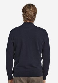 Mörkblå tröja i mjukt material med klassisk krage och lång ärm. Designen är enkel med en figursydd silhuett och ribbad nederkant.