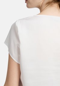 Weiße Bluse mit kurzen, fließenden Ärmeln und einem glatten, leichten Stoff. Der Rücken zeigt ein einfaches, sauberes Design.