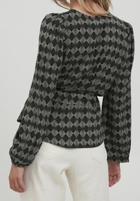 Blusa a fantasia bianca e nera con maniche lunghe e puffate e vita stretta. Presenta un motivo geometrico a ventaglio su uno sfondo scuro.