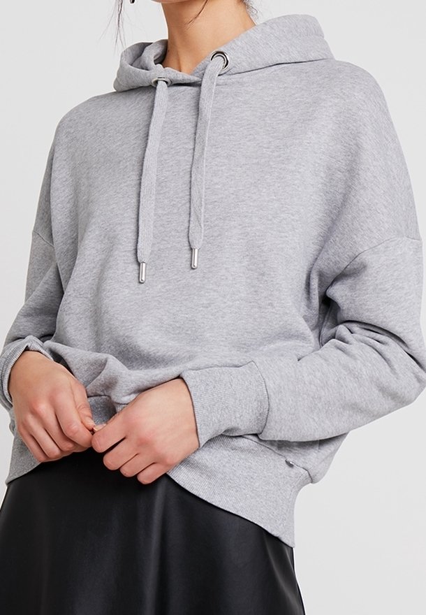 Hoodie gris en tissu doux avec capuche à cordon, poignets côtelés et coupe décontractée. Associé à une jupe en cuir noir.