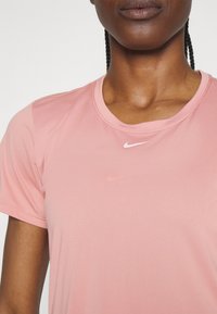 Camiseta deportiva Nike de color rosa, con manga corta, cuello redondo, textura suave y pequeño logo blanco en el pecho.