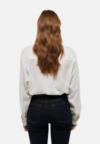 Blouse ivoire à manches longues avec une coupe décontractée, dotée d'un empiècement au dos, assortie à un jean taille haute en denim foncé et à des accents de boutons.