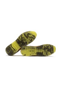 Las suelas de los zapatos presentan un material amarillo translúcido con una superficie texturizada. Los patrones en negro y gris incluyen un detalle de un paisaje urbano.