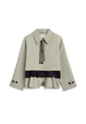 Beige cropped jack met brede kraag, zwarte trekkoordsluiting, zwart gelaagd paneel eronder en geruite manchetten aan lange mouwen.