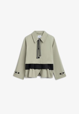 Beige cropped jack met brede kraag, zwarte trekkoordsluiting, zwart gelaagd paneel eronder en geruite manchetten aan lange mouwen.
