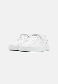 Baskets blanches en matériau synthétique, avec un design à lacets et une sangle Velcro, dotées d'une semelle texturée et d'un logo sur le côté.