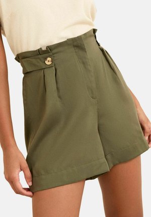 Olijfgroene shorts met hoge taille, paperbag taille, knoopsluiting en zijplooien, gedragen door een model met een licht beige top.