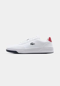 Sneaker bianca Lacoste con tomaia in pelle liscia, accento di tacco rosso a contrasto, logo grigio e suola in gomma nera texturizzata.