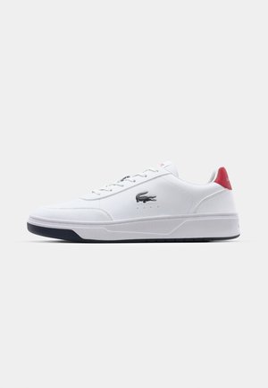 Lacoste fehér sneaker sima bőr felsőrésszel, kontrasztos piros sarkú akcentussal, szürke logóval és struktúrált fekete gumitalppal.