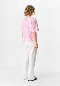 Haut rose à manches courtes avec broderie florale blanche, ouverture en forme de clé au dos, associé à un pantalon large blanc et des chaussures plates noires.