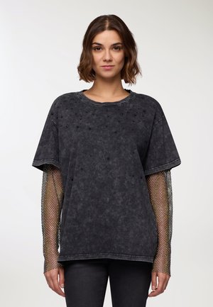 T-shirt nera oversize a maniche corte con pois testurizzati e maniche lunghe in rete, caratterizzata da una vestibilità rilassata e scollatura rotonda.