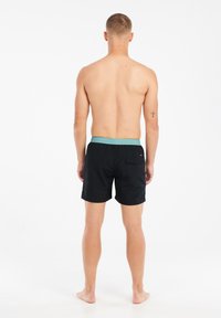 Zwarte zwemshorts met een elastische turquoise tailleband, voorzien van een achterzak. Gladde textuur, lengte boven de knie en geen zichtbare patronen.