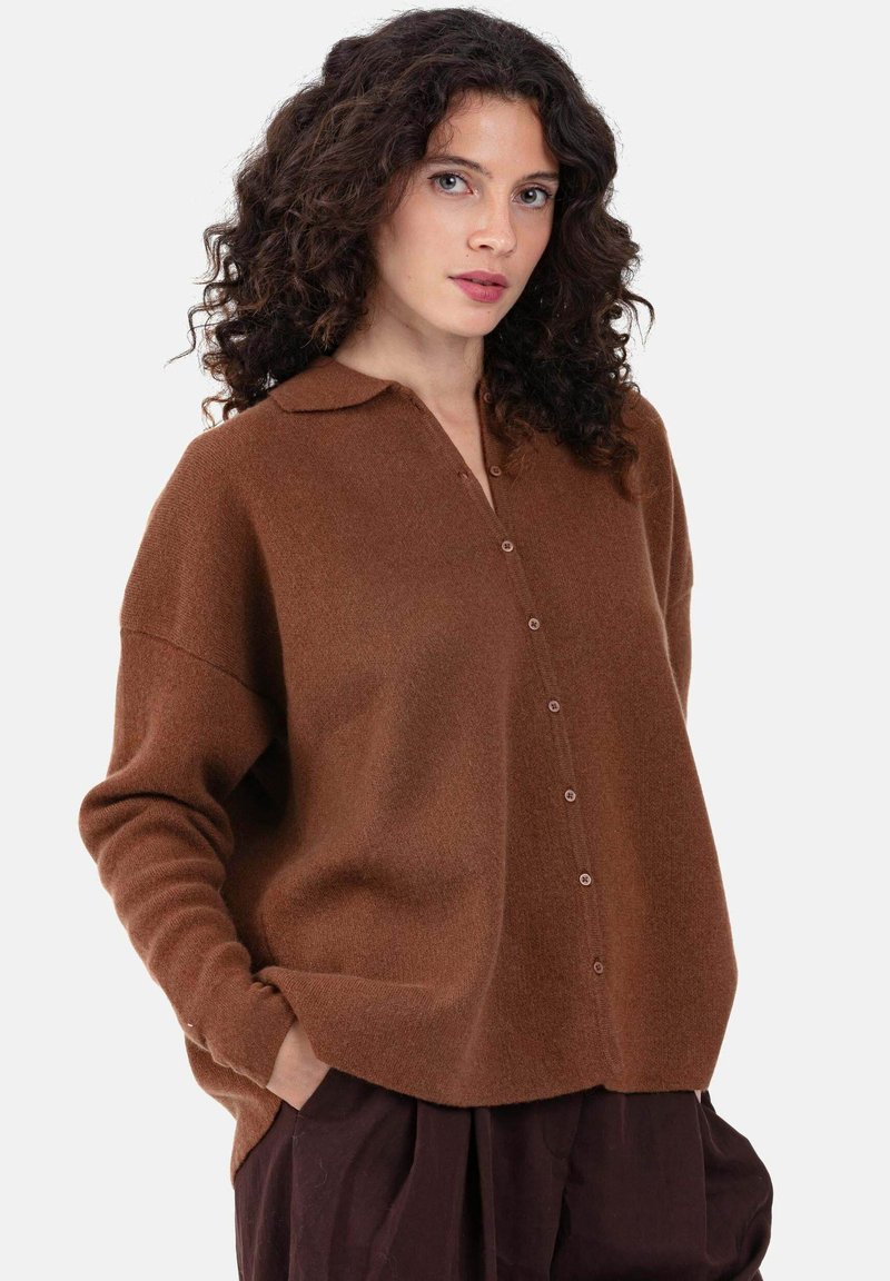 Cardigan marron en mélange de laine avec un col à revers, des boutons sur le devant, des épaules tombantes et des poches latérales. Texture douce et coupe décontractée.