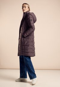 Puchowa kurtka do kolan w ciemnofioletowym kolorze z kapturem, kieszeniami po bokach oraz fakturowanym, pikowanym wzorem. Połączona z dżinsami o szerokich nogawkach i białymi trampkami.