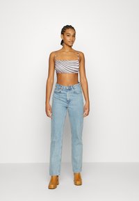 Top cropped riscado em roxo e branco, combinado com jeans de cintura alta em azul claro e botas de salto castanhas. Fundo simples.