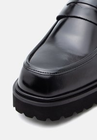 Fekete bőr loafer, fényes felülettel, kerek orral, varrott részletekkel és vastag, texturált gumitalppal.