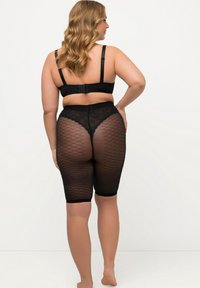 Shapewear nero con design in rete, caratterizzato da vita alta e lunghezza a metà coscia. Il materiale è liscio con dettagli in pizzo in vita.