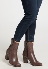 Brune læder ankelstøvler med en rund tå og en høj blokhælhæl. Har en sidelukning med lynlås og et foldet design ved anklen.