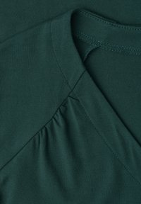 Dark green fabric with gathered detail near a round neckline and visible seam stitching on soft material.