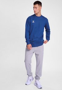 Blå långärmad skjorta i kombination med ljusgråa sweatpants. Skjortan har en liten vit logotyp; byxorna har elastiska muddar och sidofickor.