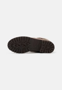 Sole di scarpa marrone con scanalature profonde, superficie testurizzata e bordi rinforzati. Presenta un logo inciso e un materiale in gomma resistente.