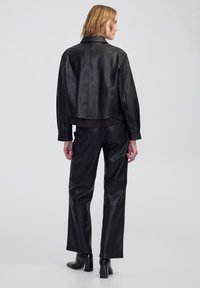 Czarna skórzana kurtka o skróconym kroju z gładką fakturą, z długimi rękawami i kołnierzem, zestawiona z czarnymi skórzanymi spodniami o wysokim stanie.