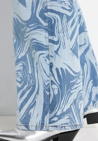 Denim flare broek met een lichtblauw abstract patroon, gestructureerde stof en contrasterende stiksels. Gecombineerd met glanzende zilveren block-heeled schoenen.
