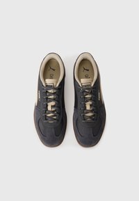 Ein Paar schwarze und beige Puma-Sneaker mit Schnürsenkeln, von oben auf einem weißen Hintergrund betrachtet.