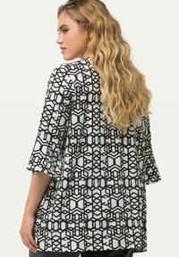 Schwarz-weiße Tunika mit geometrischem Muster und Dreiviertelärmeln, die einen lockeren Schnitt und eine weiche Textur aufweist.
