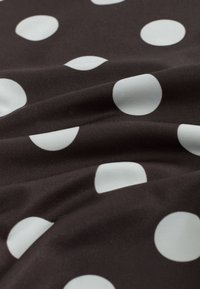 Gros plan d’un tissu noir avec de grands pois blancs uniformément espacés et une texture et des plis visibles.