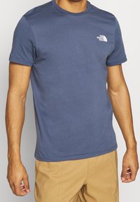 Modré bavlněné tričko s krátkými rukávy a kulatým výstřihem. Na levé straně hrudníku je malé bílé logo. Hladký povrch, běžný střih.