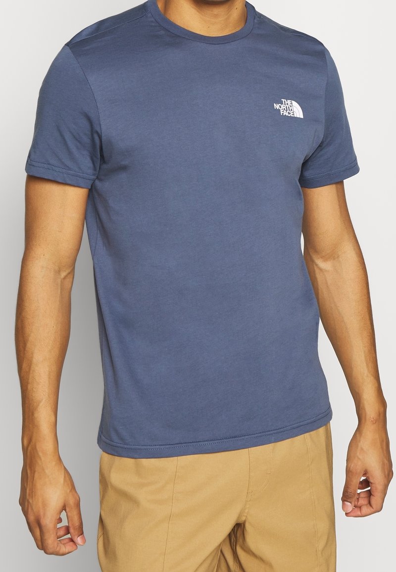 Modré bavlněné tričko s krátkými rukávy a kulatým výstřihem. Na levé straně hrudníku je malé bílé logo. Hladký povrch, běžný střih.